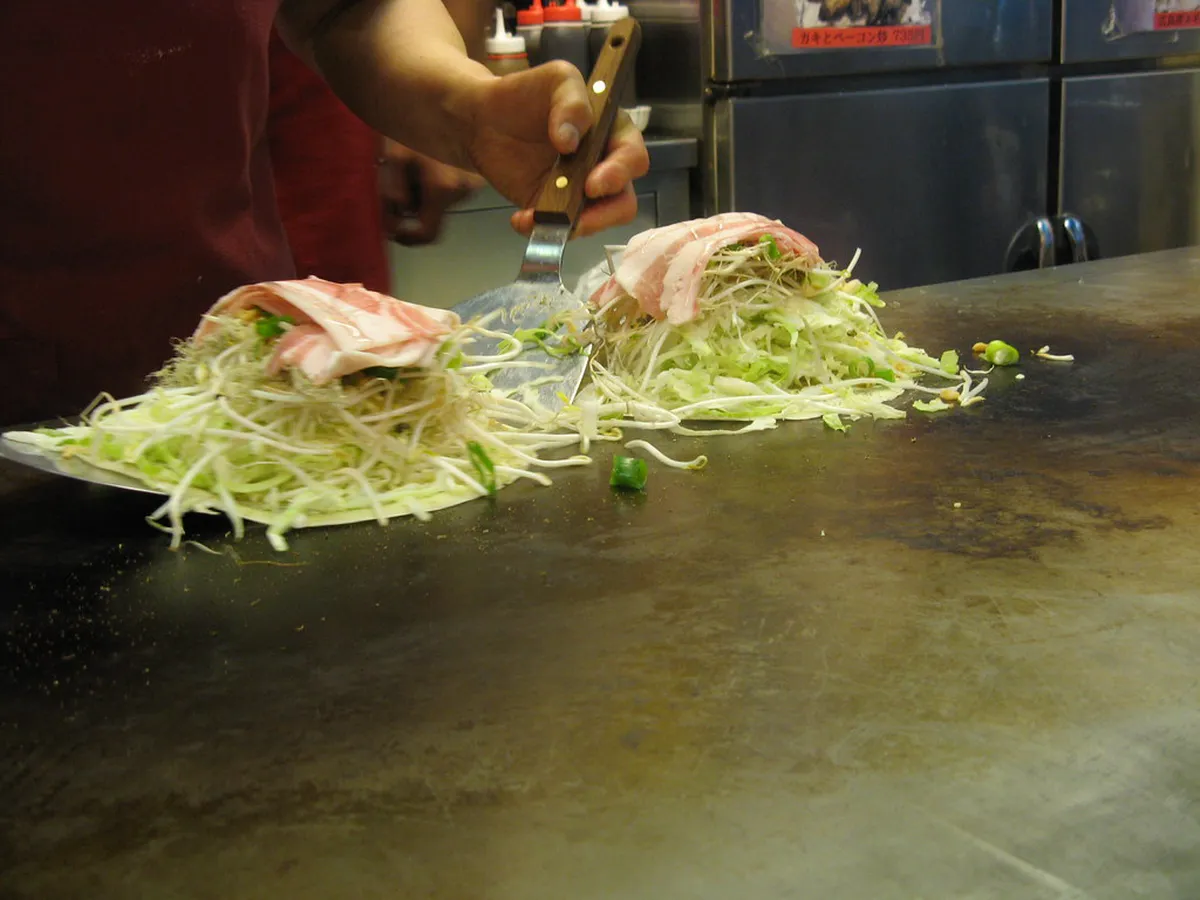 Hiroshima-style okonomiyaki layered pancake being prepared on a hot iron griddle in Japan