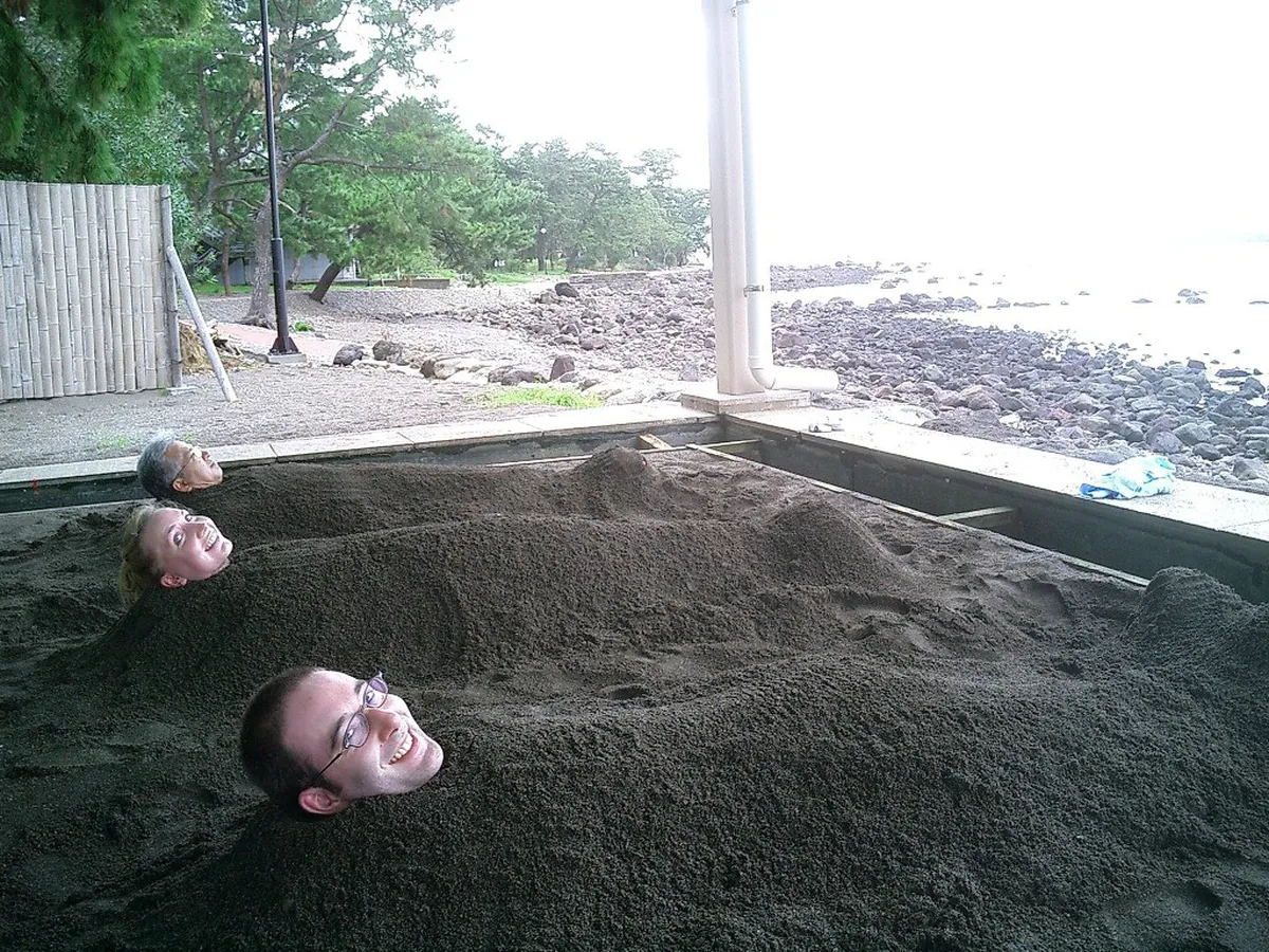Visitors enjoying Beppu sand bath on the beach in Japan, buried in warm volcanic sand by the sea
