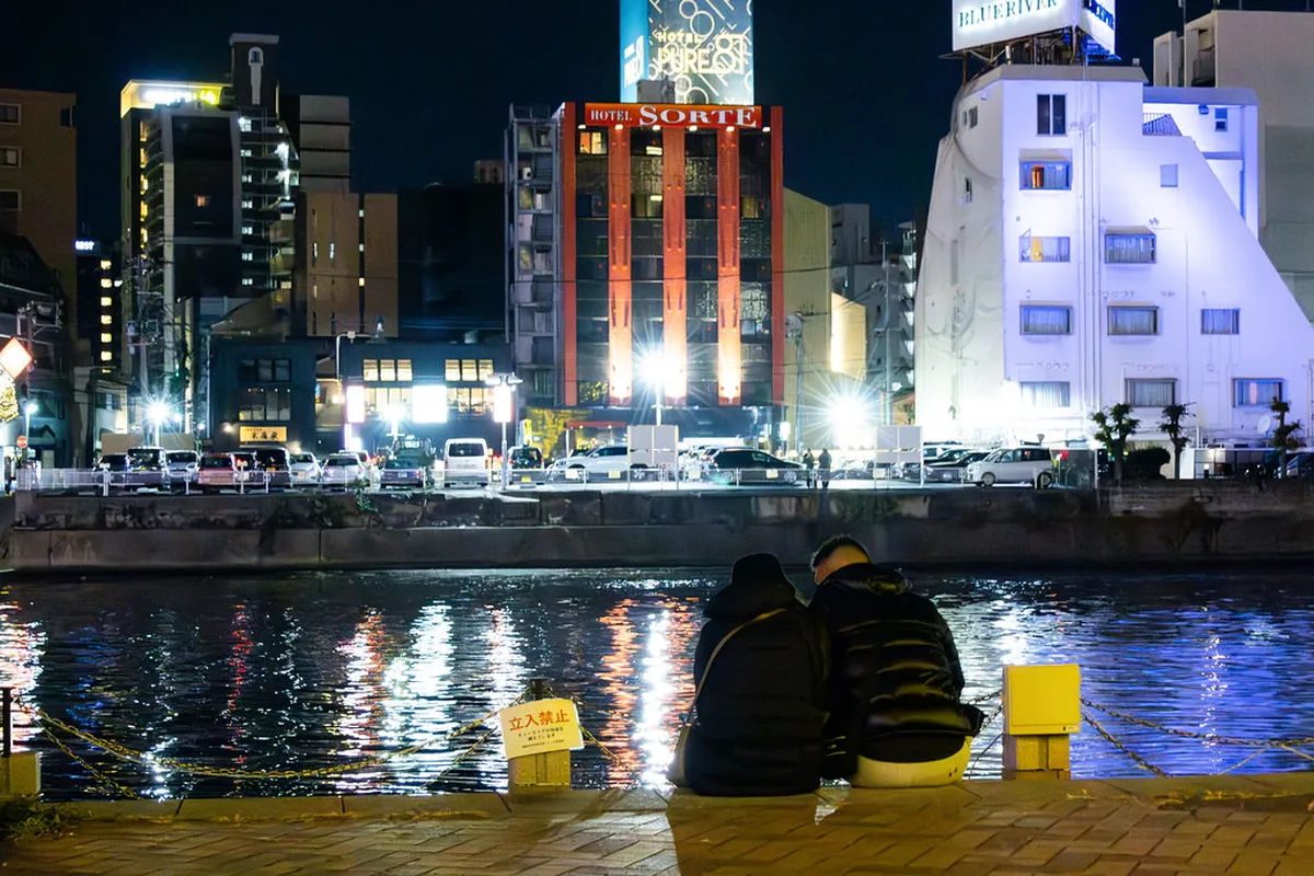 Nakasu riverside in Fukuoka at night with colorful neon reflections on the water and vibrant street life, Japan
