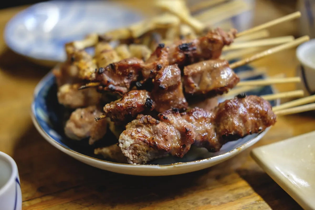 Grilled meat skewers with charred exterior and juicy interior, arranged on a wooden board at an izakaya counter