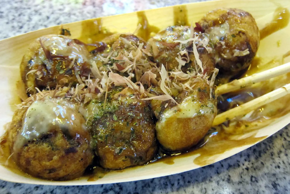 Osaka street food stalls along Dotonbori with crowds enjoying takoyaki and other snacks, Japan