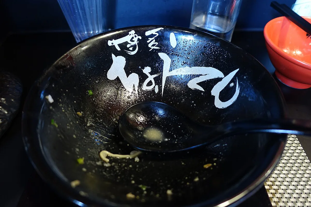 Bowl of Hakata tonkotsu ramen beside glowing yatai stalls at dusk, Japan — 1