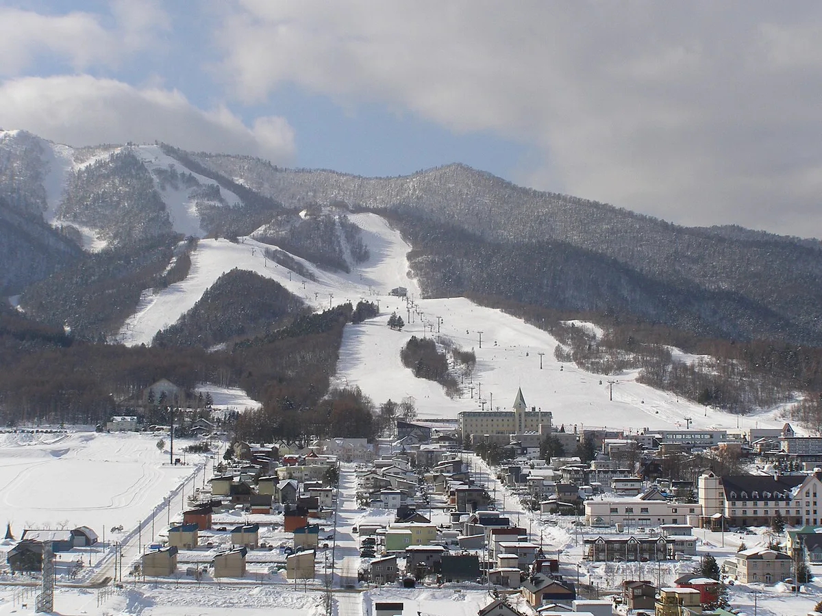 Skier descending a snowy run above Furano with mountain views, Japan — 1