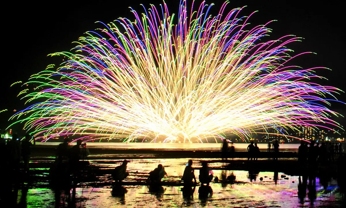 Brilliant fireworks bursting over the water near Miyajima Island and the iconic Itsukushima Shrine torii gate in Hiroshima, Japan
