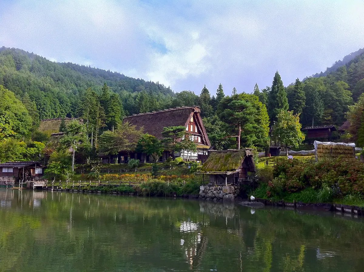 Visitors walking the gravel paths through the open-air Hida Folk Village museum with thatched farmhouses and mountain scenery in Takayama, Japan