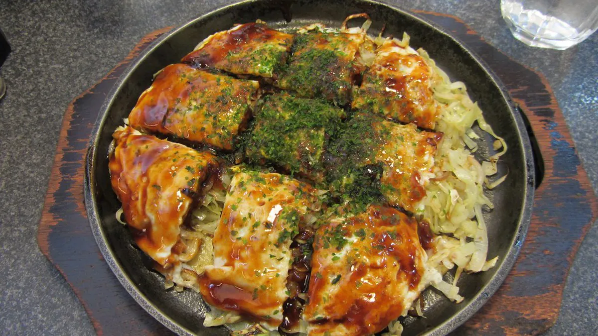 Hiroshima-style layered okonomiyaki sizzling on a teppan grill at a local restaurant in Japan