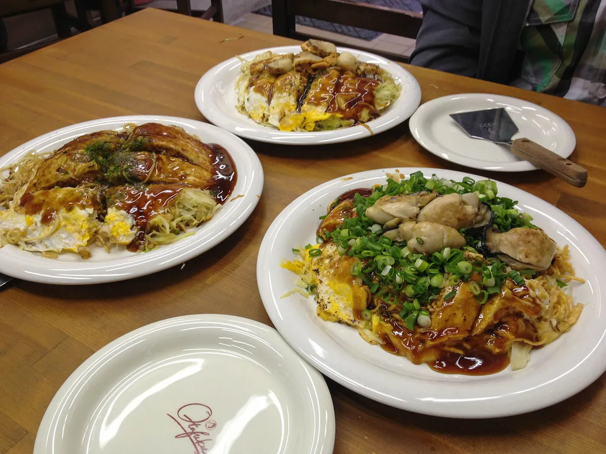 Hiroshima-style okonomiyaki being cooked on a teppan grill with noodles, cabbage and egg layers in Japan