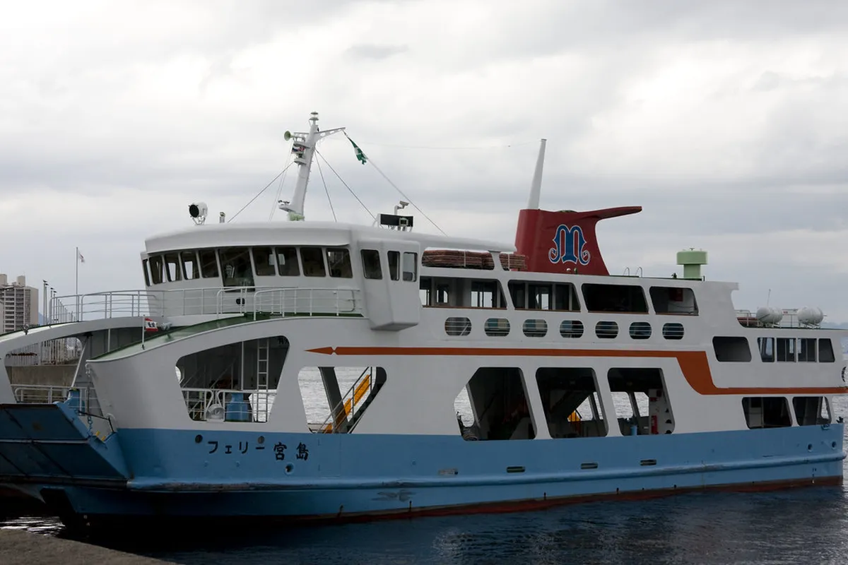 Miyajima ferry crossing with passengers approaching Itsukushima Shrine on a calm day in Hiroshima, Japan