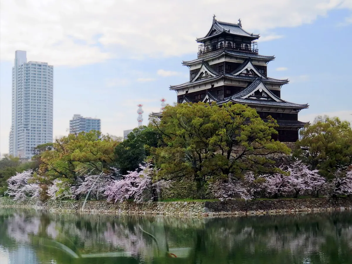 Hiroshima castle keep rising above the moat with stone walls and traditional black wooden facade, Japan