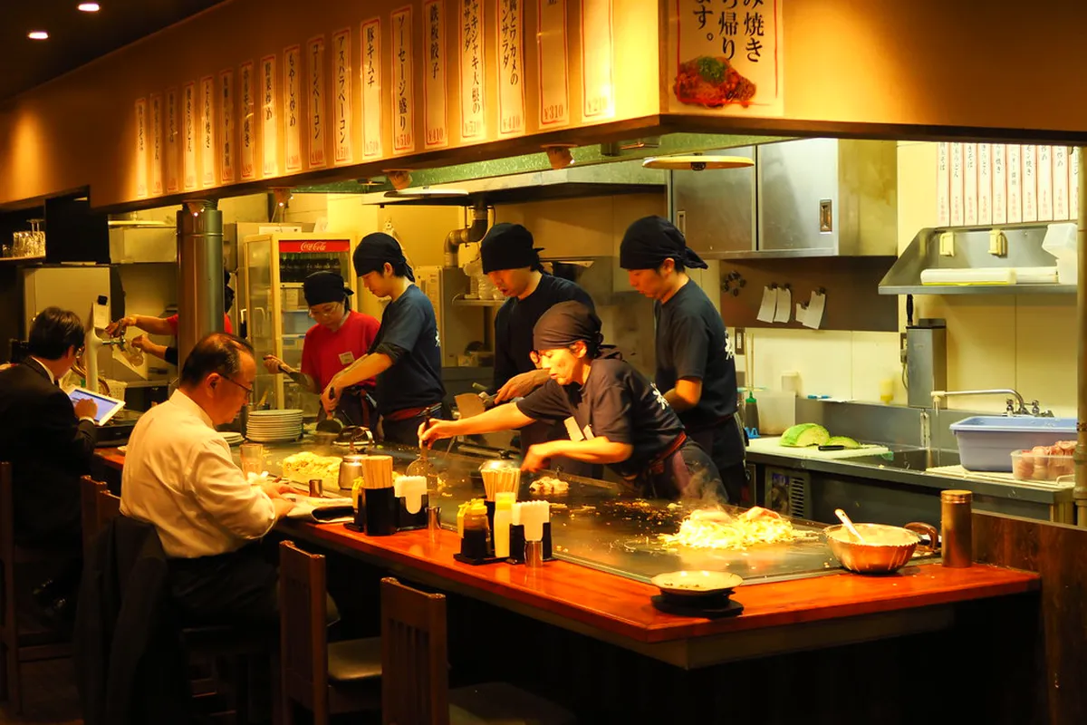 Hiroshima-style okonomiyaki being cooked on a teppan grill at an affordable restaurant in Japan