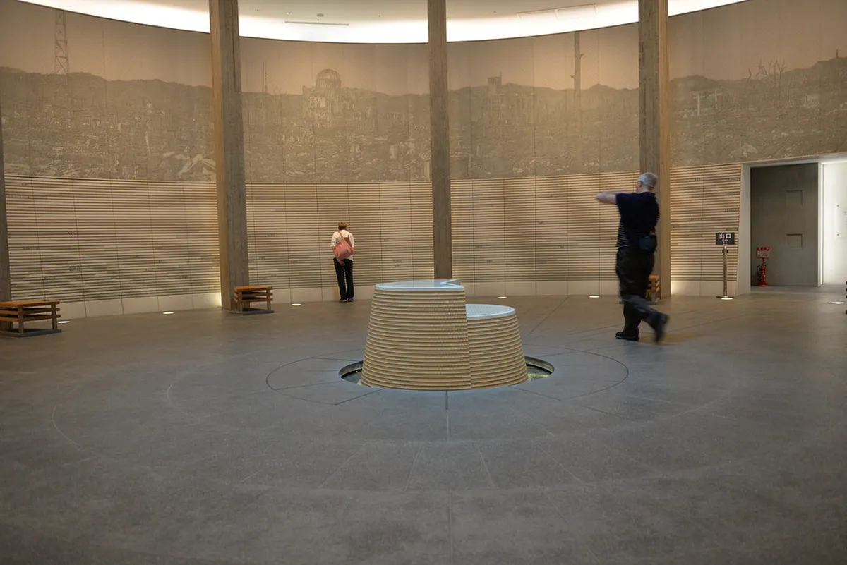Interior gallery of Hiroshima Peace Memorial Museum with dimly lit exhibits and visitor silhouettes, Japan