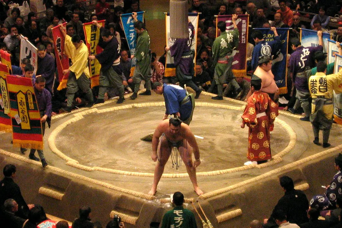 Interior view of a sumo arena with the clay dohyo ring in the center and tiered seating filled with spectators, Japan