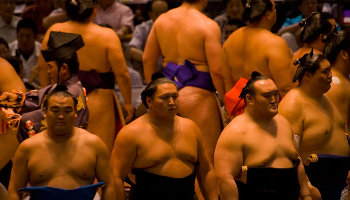 Professional sumo wrestlers competing in a tournament bout inside a Japanese arena with a packed audience