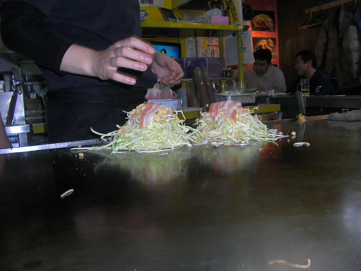 Teppan grill counter at a Hiroshima okonomiyaki stall with a chef cooking the layered pancake, Japan