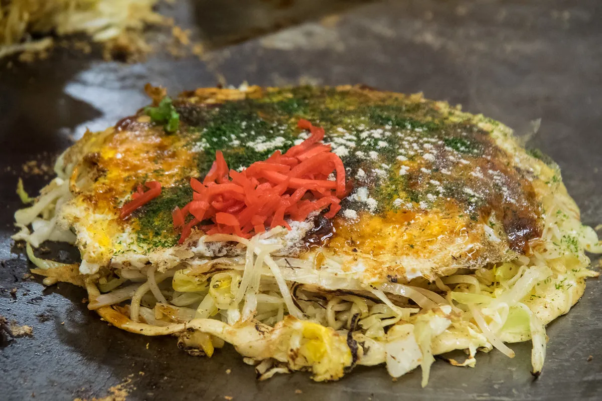 Hiroshima-style okonomiyaki with distinct layered construction on a hot teppan griddle in Hiroshima, Japan
