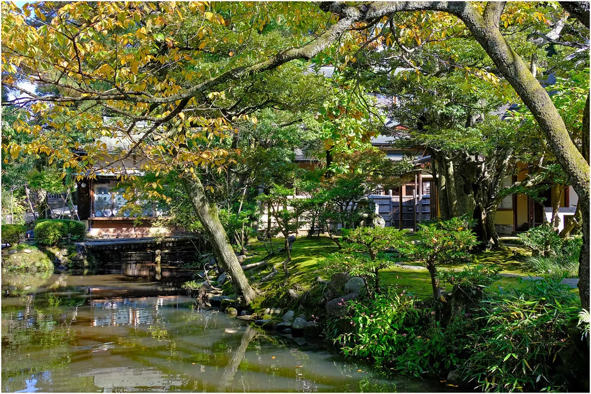 Kenroku-en garden with ancient pine trees and traditional stone lantern beside a pond in Kanazawa, Japan