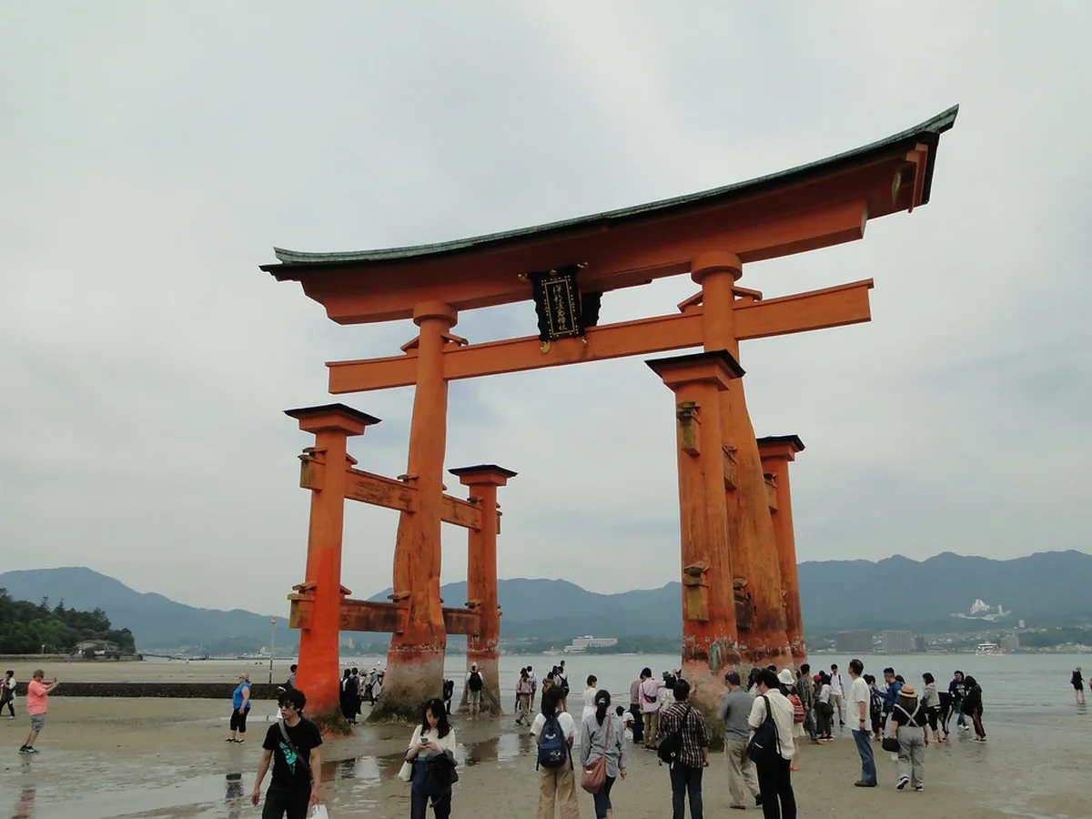 Photographer capturing the iconic vermillion torii gate reflection on the water at Miyajima Japan