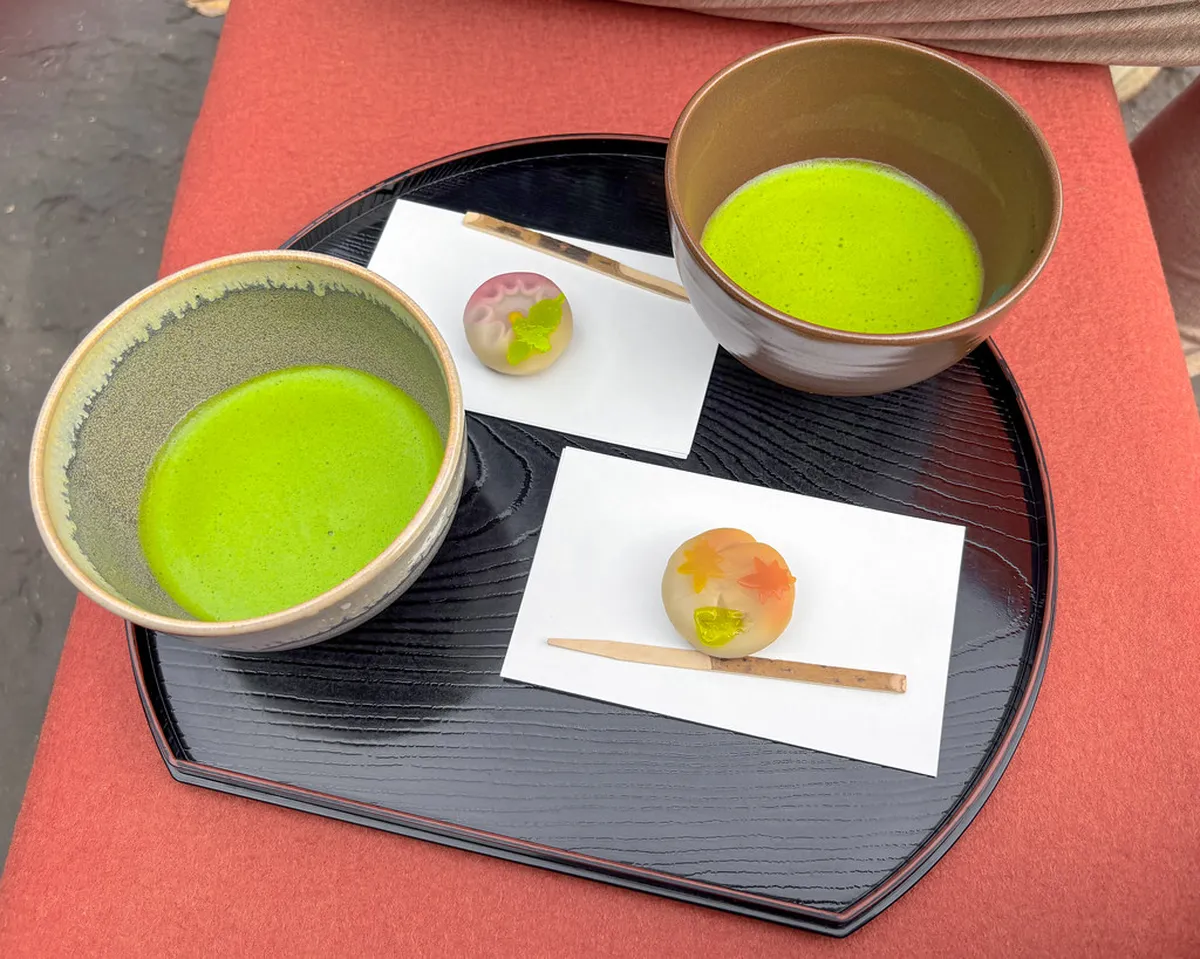 Hands holding a ceramic matcha bowl with a seasonal wagashi sweet on a tatami mat during a Japanese tea ceremony in Kanazawa, Japan