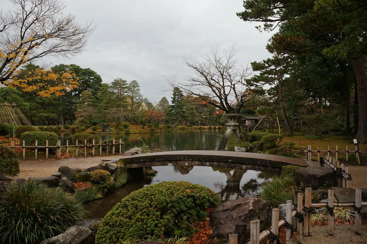 Serene pond and manicured pine trees of Kenrokuen Garden reflecting autumn colors in Kanazawa, Japan