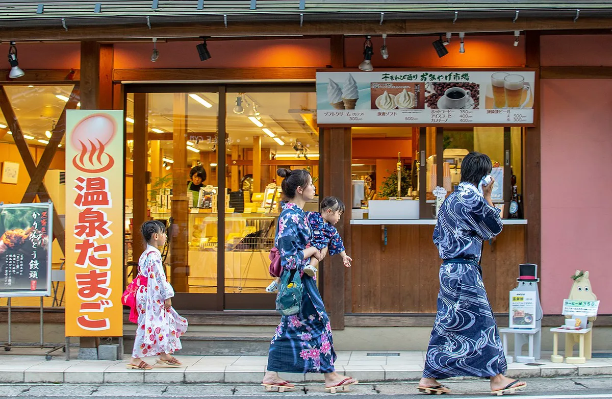 Visitors in yukata snacking along the Otani River street food stalls in Kinosaki Onsen, Japan — 2