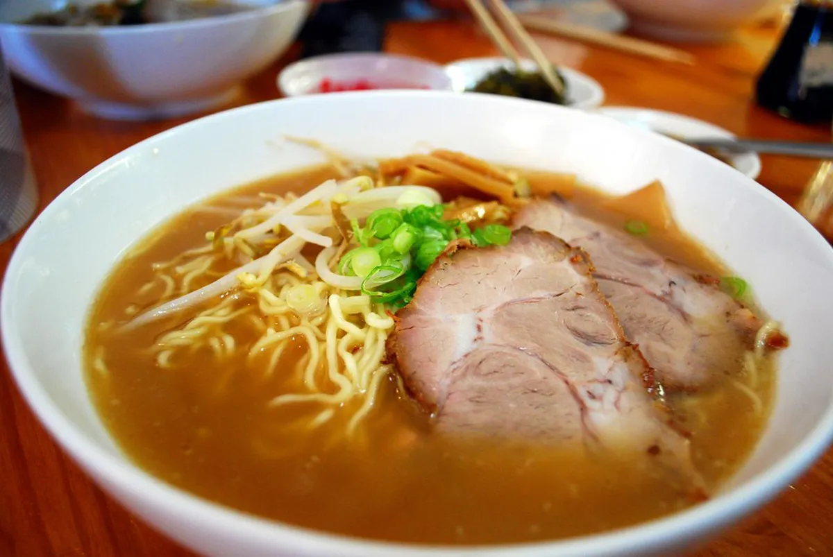 A rich tonkotsu ramen bowl with thick noodles, pork slices, and dark garlic oil floating on the broth in Japan