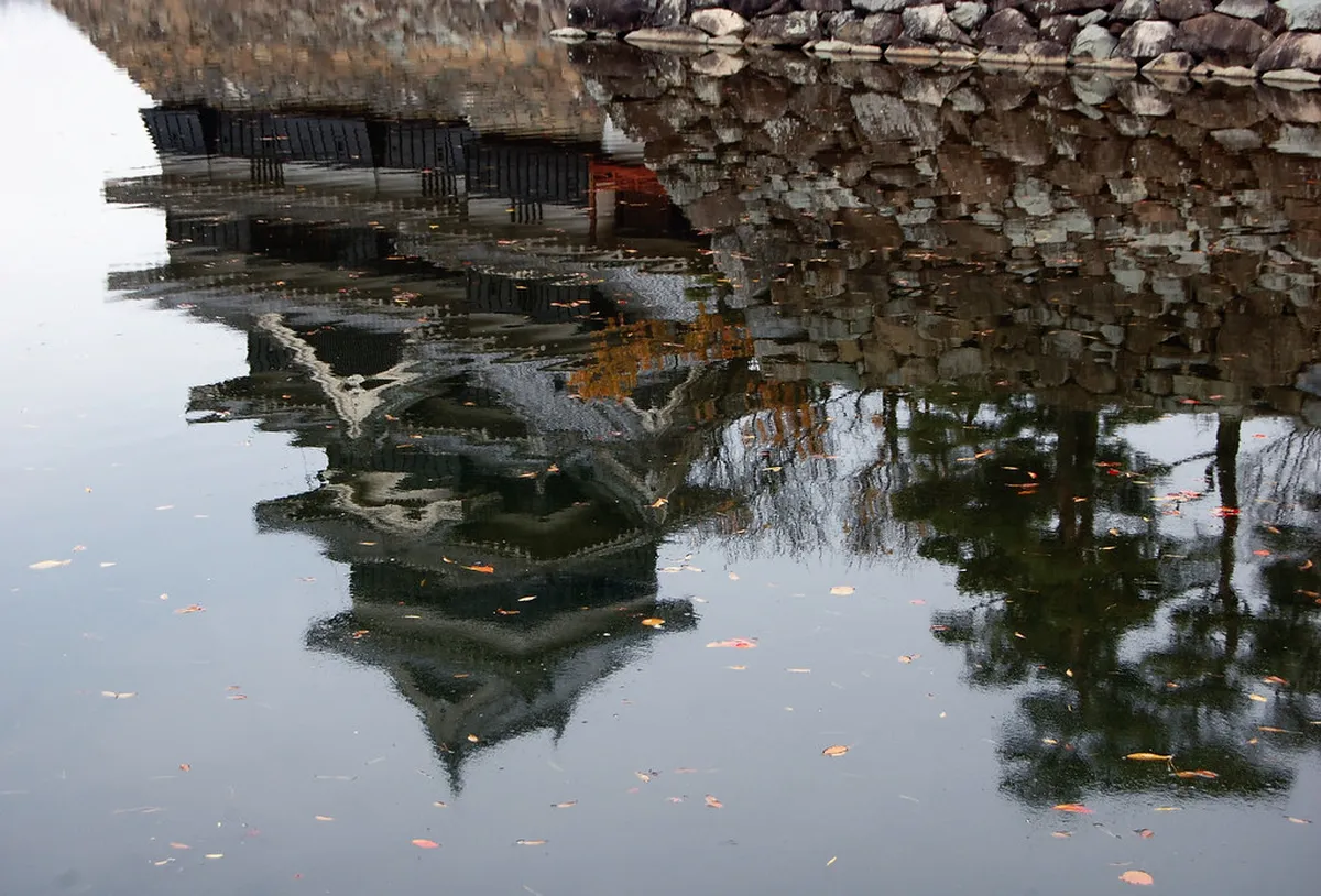 Matsumoto Castle black exterior reflected in the surrounding moat in Nagano with autumn trees framing the feudal keep