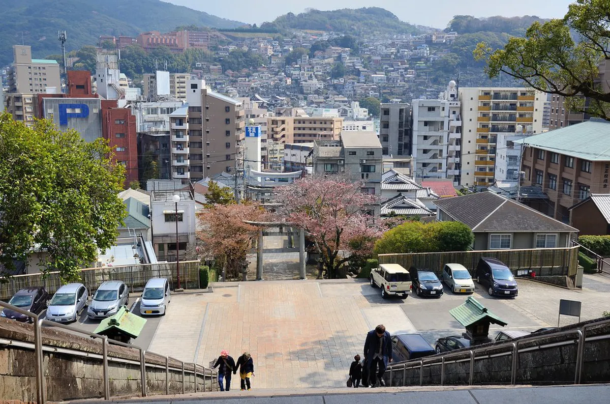 Suwa Shrine stone staircase with vermilion torii gates winding up the forested hillside in Nagasaki, Japan