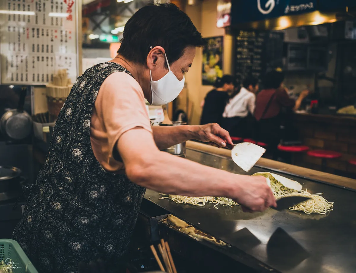 Layered Hiroshima-style okonomiyaki being cooked on a hot iron teppan griddle at a restaurant in Japan
