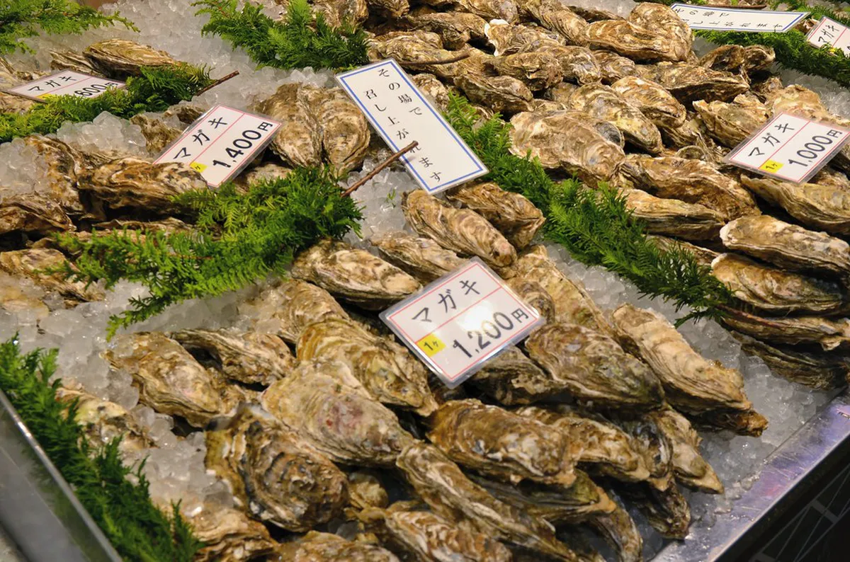Live oysters and fresh seafood displayed on ice at a vendor counter inside Omicho Market Kanazawa
