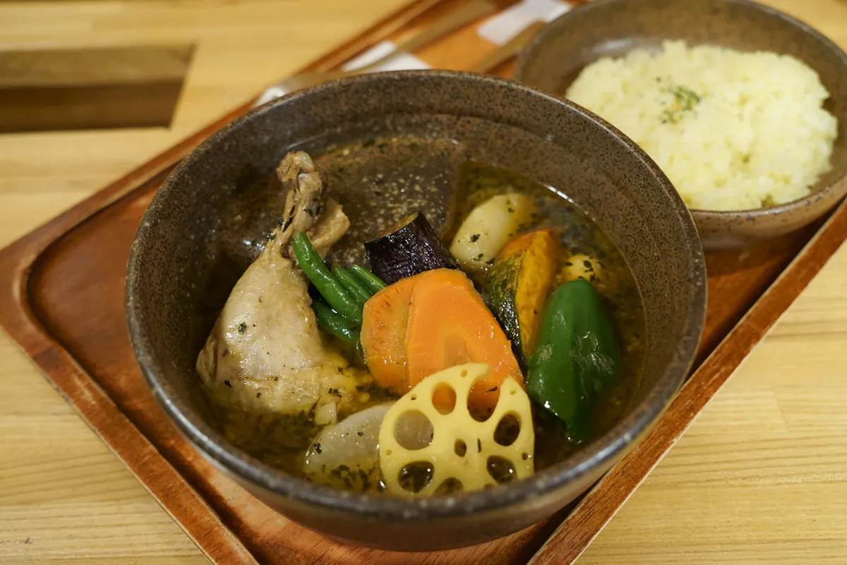 Sapporo soup curry with thin spicy broth loaded with crispy flash-fried vegetables and bone-in chicken over rice in Hokkaido Japan