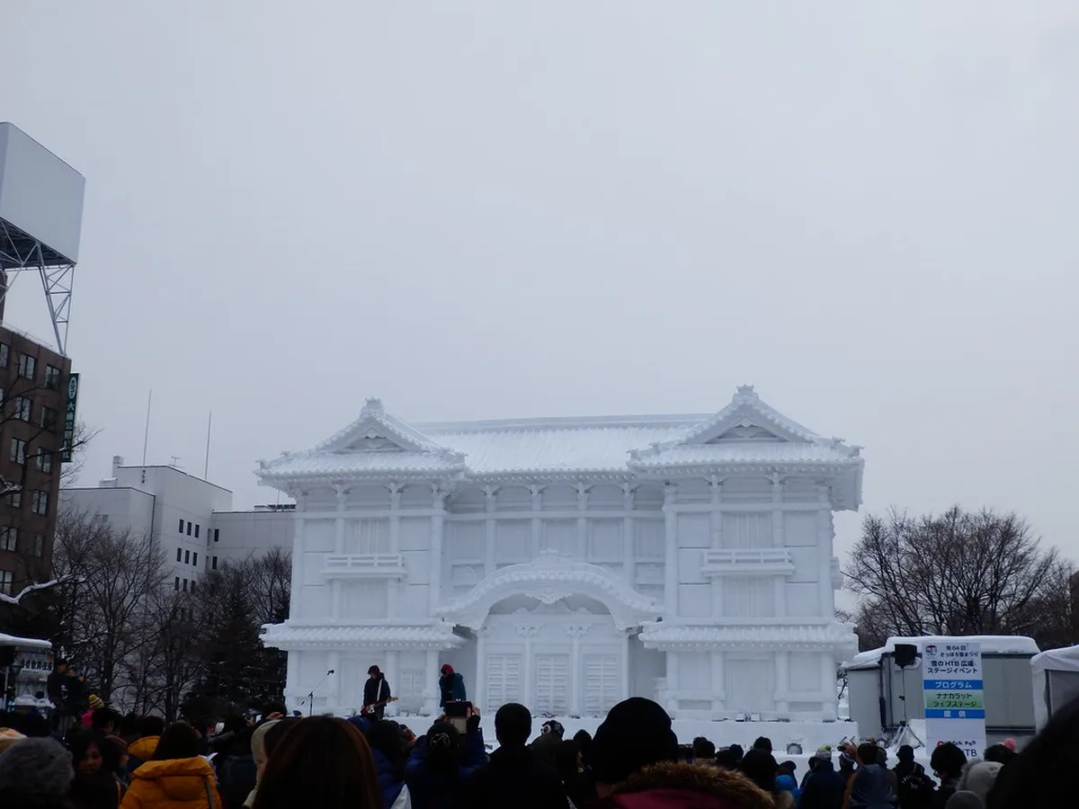Crowds walking past enormous illuminated snow sculptures along the snow-lined boulevard of Sapporo's Odori Park in Japan