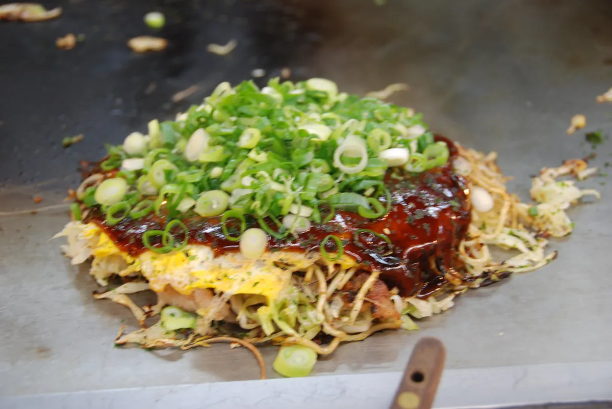 A chef preparing Hiroshima-style layered okonomiyaki on a teppan grill in Hiroshima, Japan