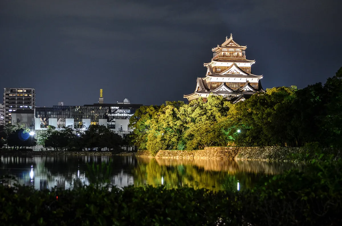 Hiroshima Castle’s five-storey wooden keep reflected in the moat surrounded by autumn foliage and blue sky in Japan