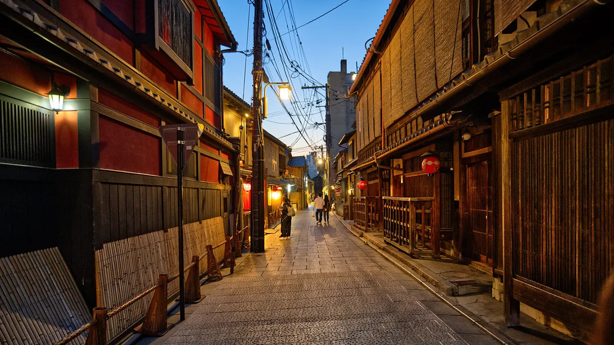 Lantern-lit Hanamikoji Street in Gion district at dusk with traditional wooden machiya townhouses lining the historic road in Kyoto, Japan