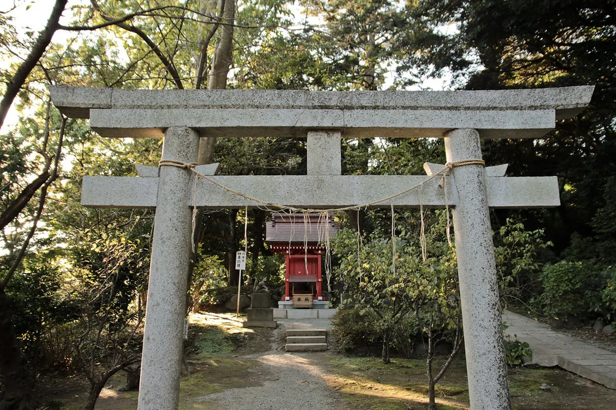 Torii gate entrance to a Shinto shrine surrounded by green trees in Kamakura, Japan