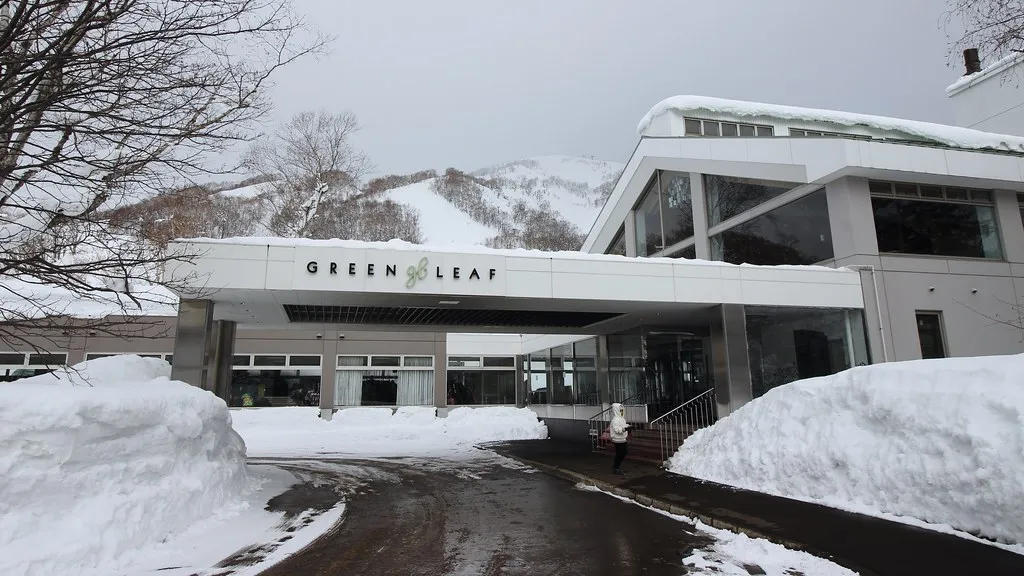 The Green Leaf Niseko Village hotel exterior with modern architecture set against forested Niseko slopes