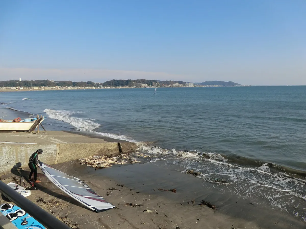 Surfers riding waves at a Kamakura beach with summer huts and the Japanese coastline visible in Japan